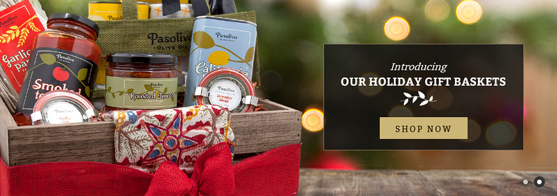 Pasolivo homepage banner — a wooden crate of preserves, oils and a tote tied with a red ribbon, with an Introducing Our Holiday Gift Baskets panel and a Shop Now button.