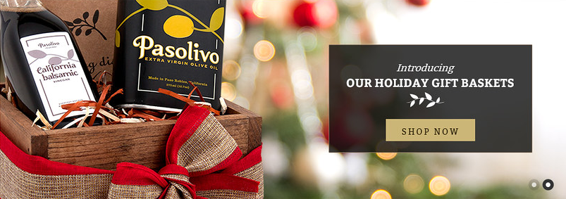 Pasolivo homepage banner, second variant — olive oil tin and California balsamic bottle in a gift crate against holiday lights, with the same Shop Now panel.